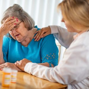 Older woman in distress with nurse assisting her. Article about signs of stroke for caregivers.