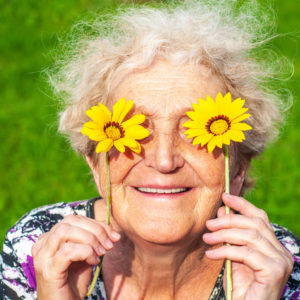 Older woman holding flowers over face. Article about aging through visual impairments.