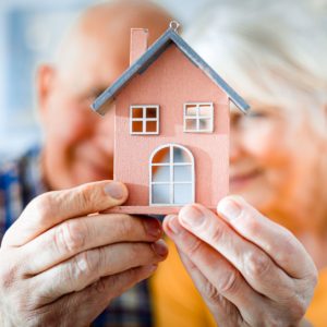 An older couple holding a model house. Cover image for article on aging in place.
