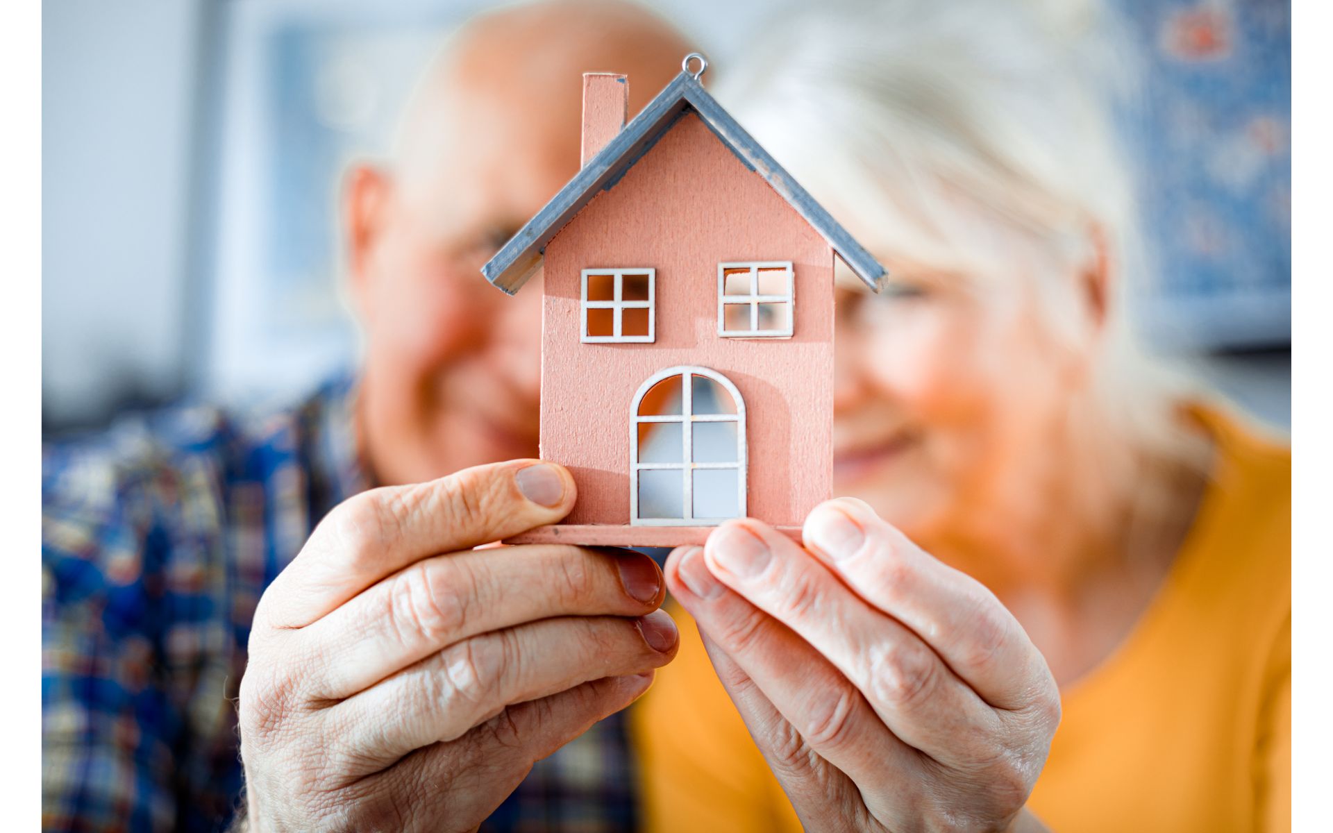 An older couple holding a model house. Cover image for article on aging in place.