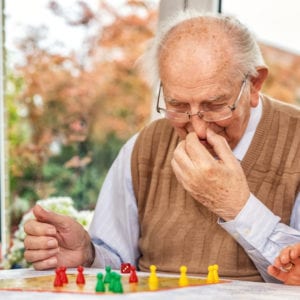 Older man playing board game. Cover image for article about games to play with older adults.