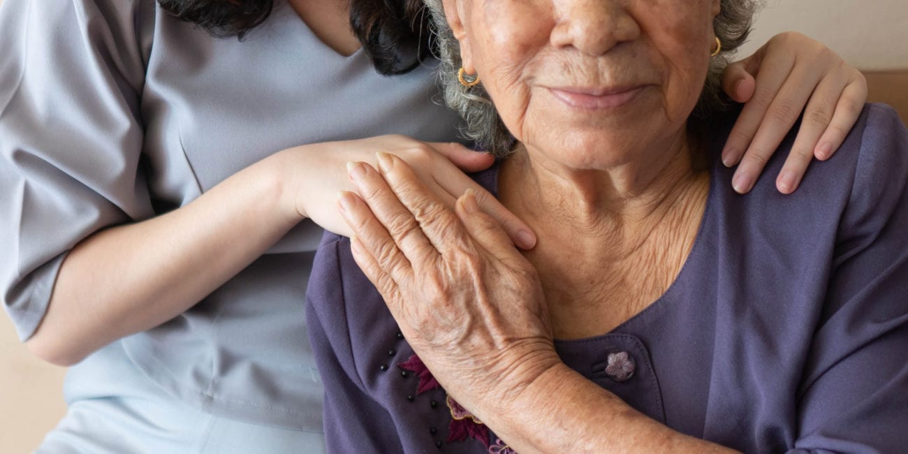 Older woman smiling with older man's hand on her shoulder.