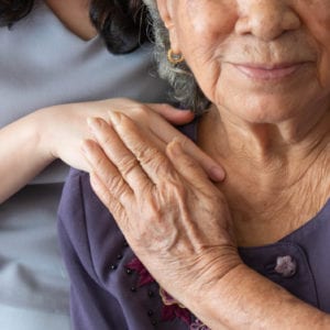 Older woman smiling with older man's hand on her shoulder.