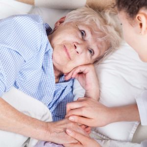 Older woman lying in bed, holding hand of loved one. Cover image for article about a deathbed rally.